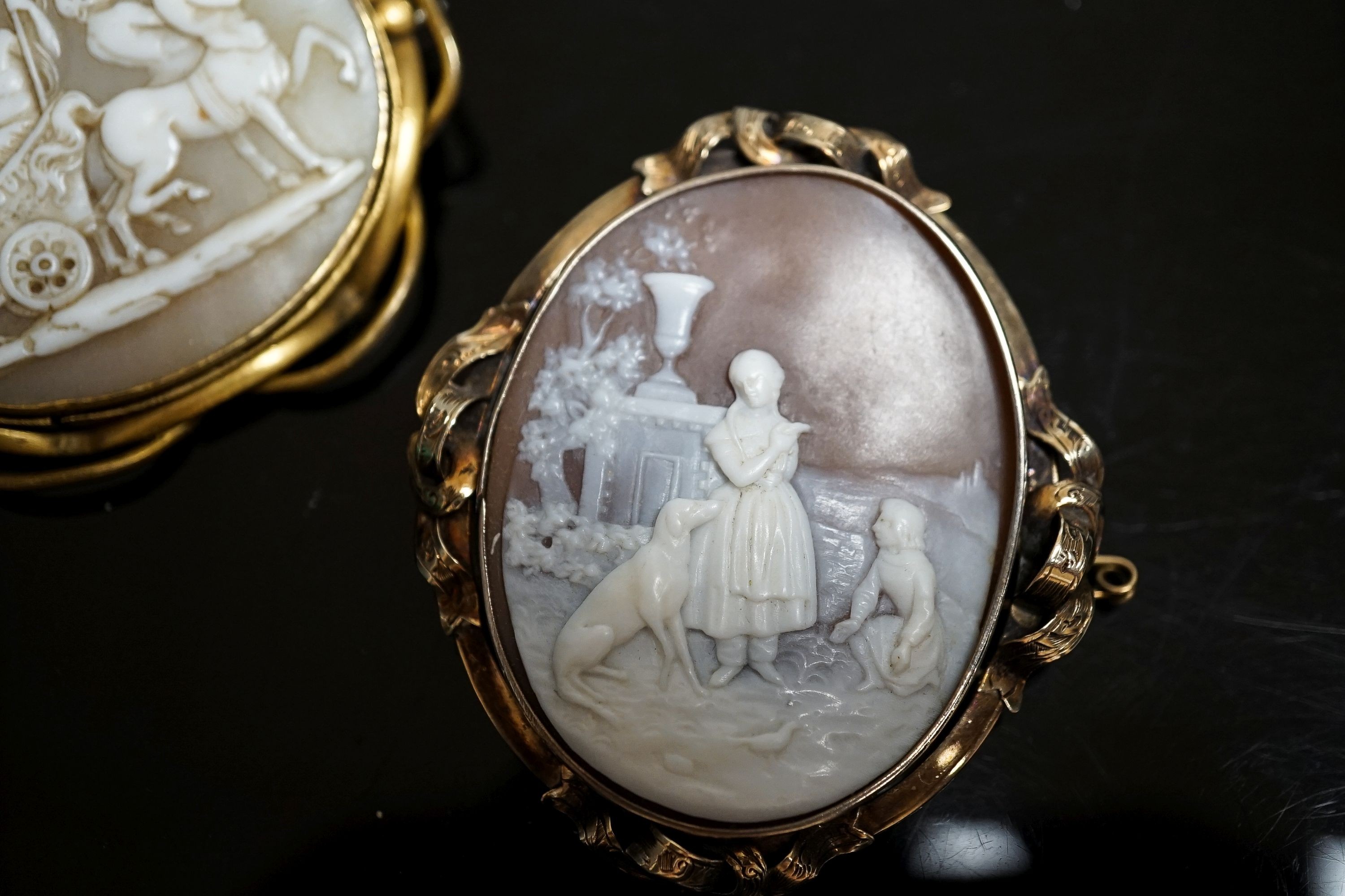 An Edwardian yellow metal mounted carved oval cameo shell and a gilt metal mounted cameo shell carved with chariot and mythical creatures, 52mm.